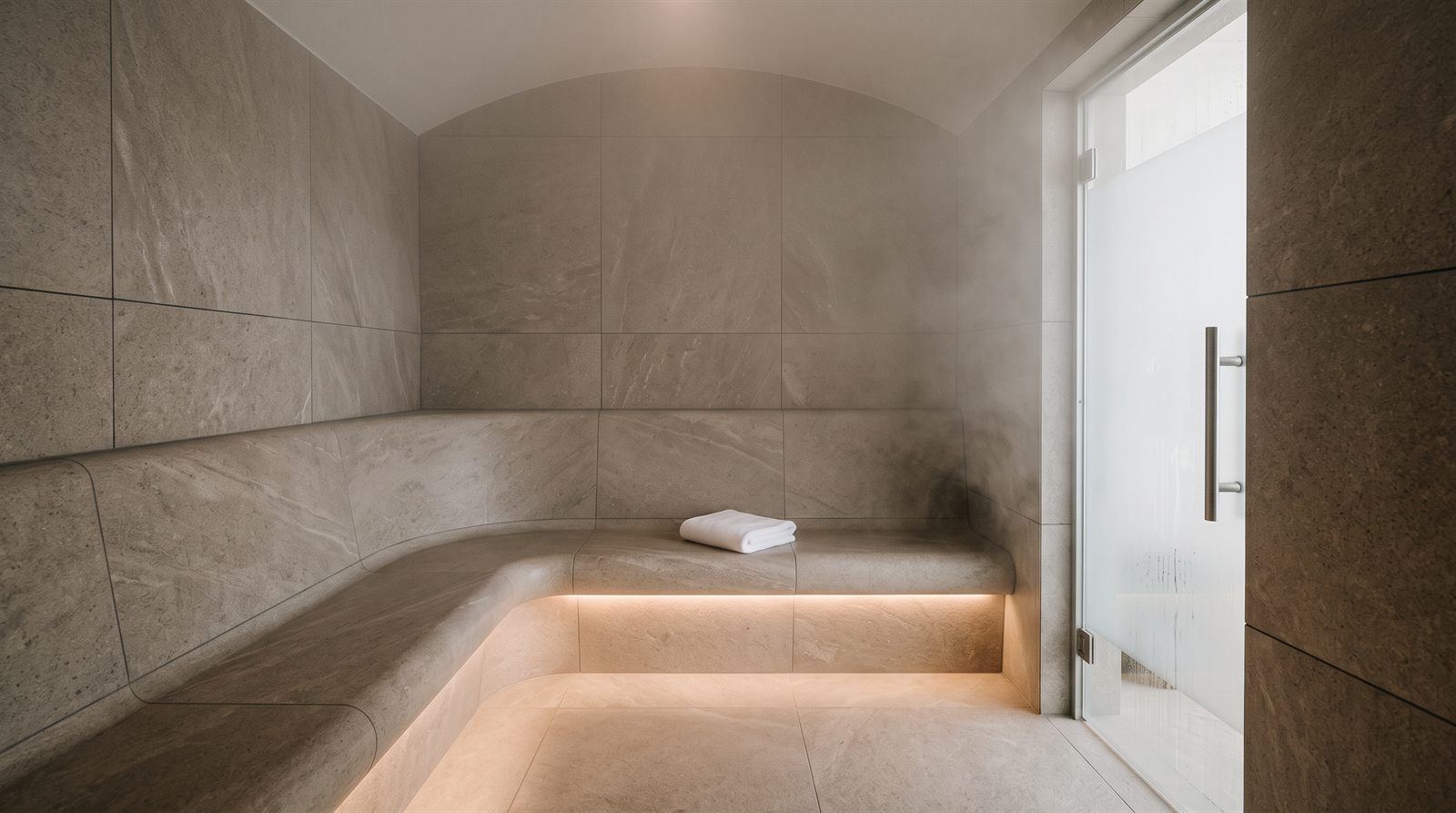 Moderní parní sauna v hotelovém wellness s lavicemi z velkoformátového kamene, jemná pára a složený ručník